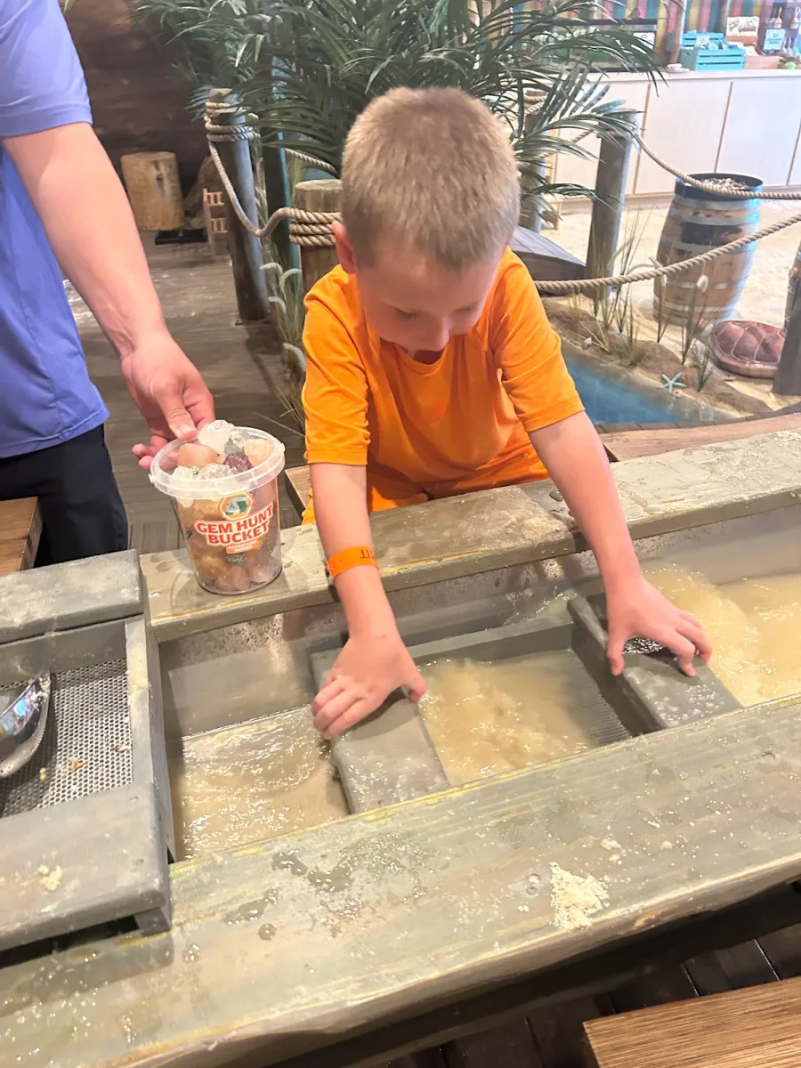 A boy sifting for gems at the mining trough with a Gem Hunt Bucket beside him