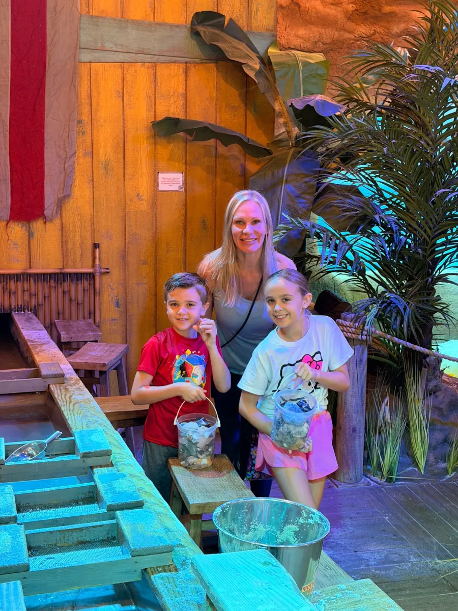 A mom and two kids holding buckets of gems beside the mining trough