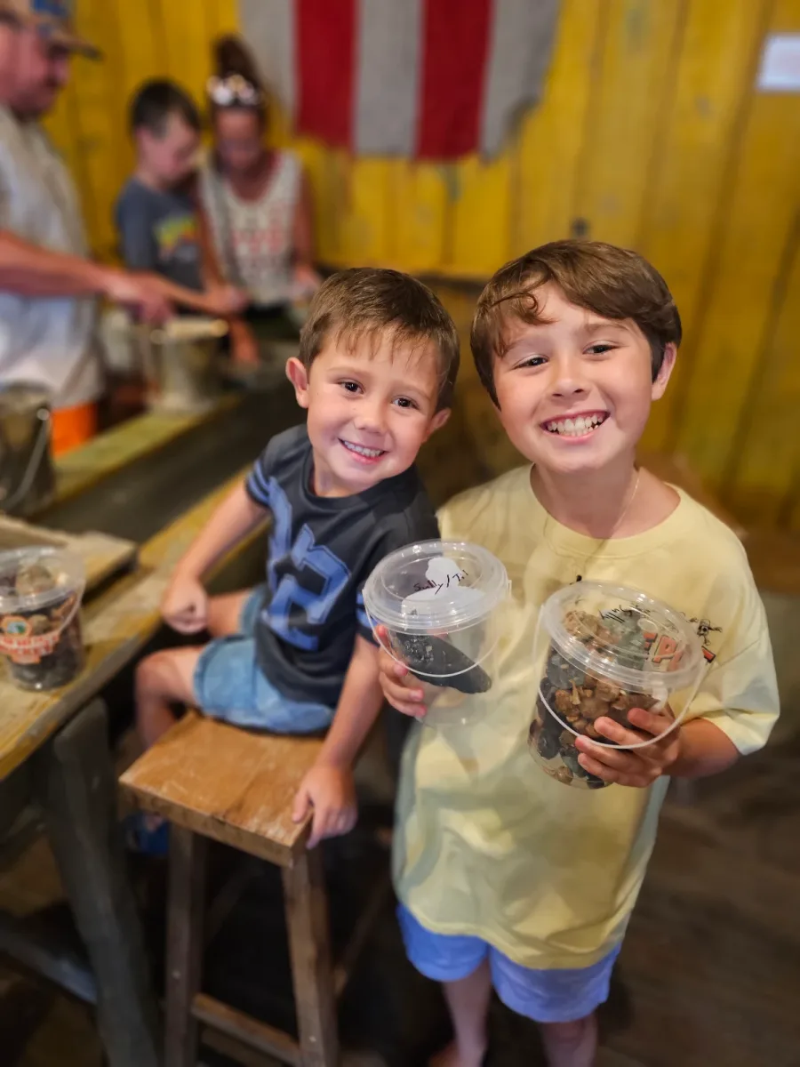 Two smiling boys holding buckets full of gems and fossils